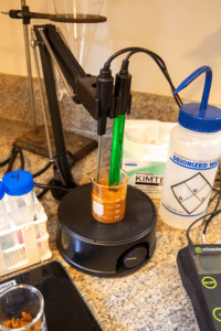 a green pH meter probe in an orange suspension of soil in water